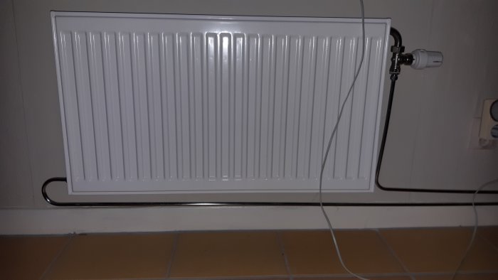 Radiatormed en anslutning på sidan och termostatventil, kablar på golvet.