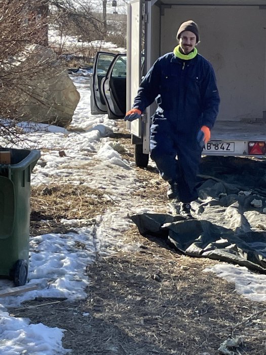 Arbetare i blått arbetsställ och säkerhetshjälm bär saneringsutrustning vid ett renoveringsprojekt utomhus.