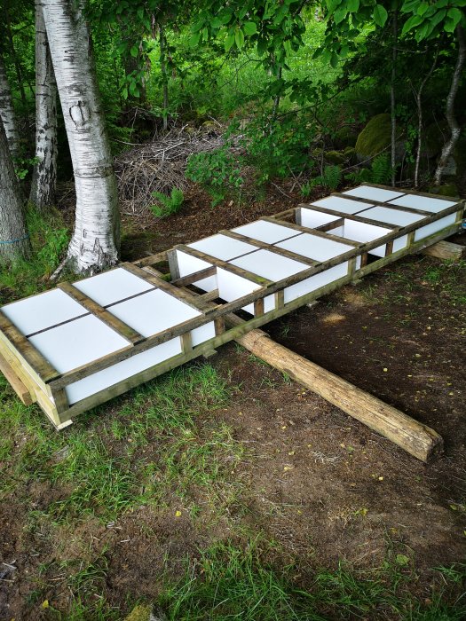 Renoveringsprojekt med cellplast monterat på träramar i trädgård, använd som isolering för byggnad.