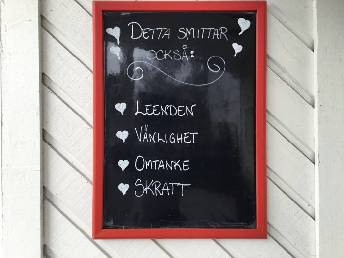 Svart anslagstavla med text "Detta smittar också: leenden, vänlighet, omtanke, skratt" i vit krita, inramad i rött.