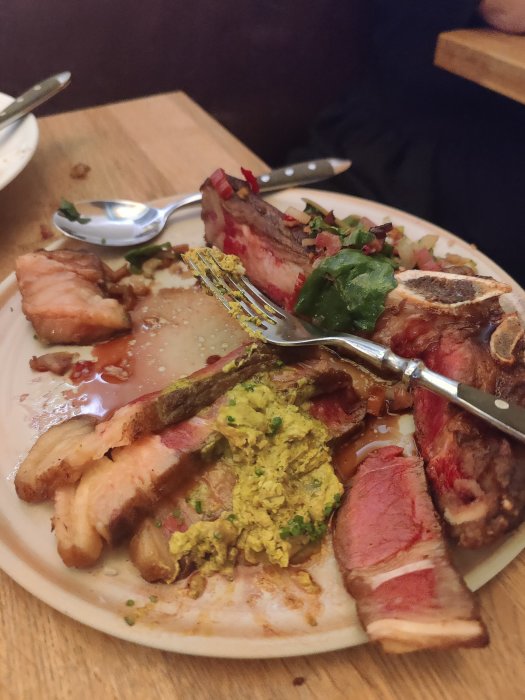 Halväten tallrik med stekt kött och kryddad röra, kniv och gaffel på sidan.