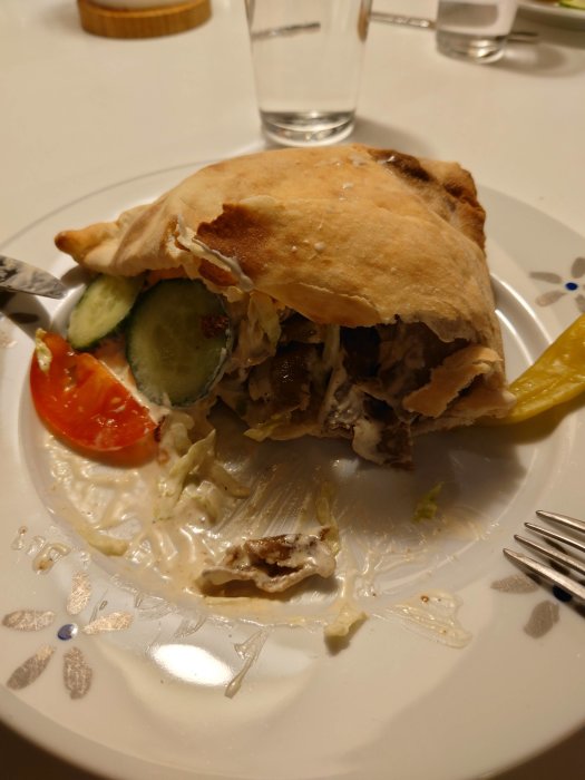 Halväten kebabrulle på tallrik med sallad, tomat och vit sås, samt vattenglas i bakgrunden.