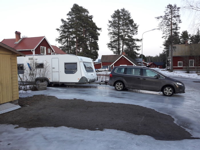 Bil står på en isig uppfart nära en husvagn med hus i bakgrunden.