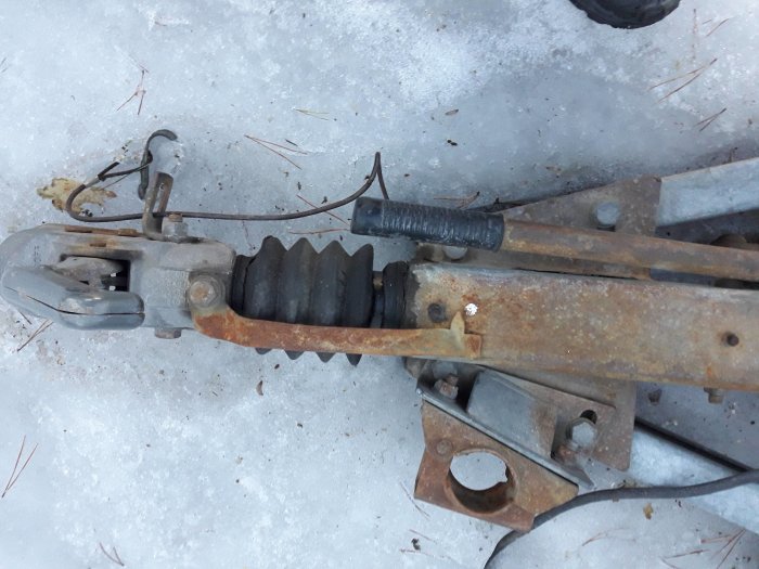 Rostig dragstång till släpvagn med märkningar ritade med spritpenna, synliga i snöig miljö.