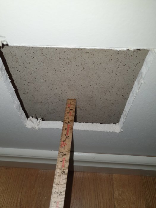 Inspektionslucka uppågad i vägg med måttsticka som visar att en vermikulitskiva finns 5 cm in.