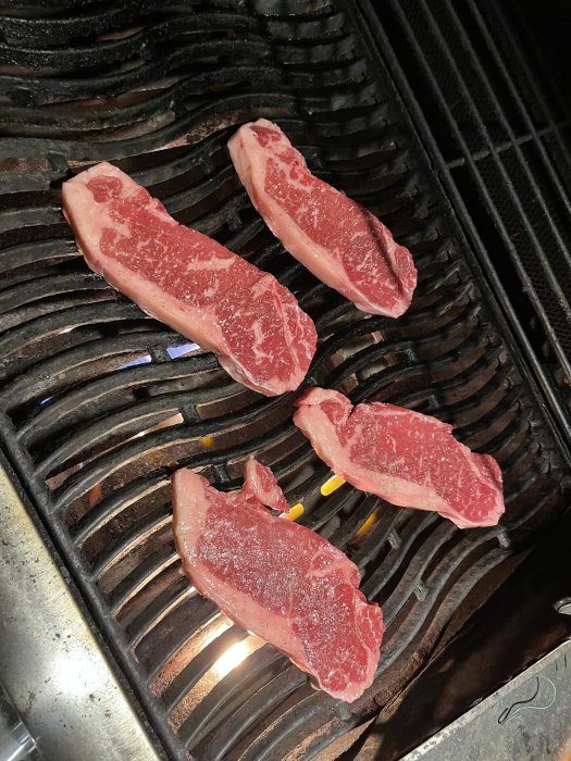 Ryggbiffar som grillas på en grill med delvis slocknade brännare.