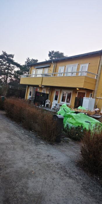 Gult radhus med balkonger på andra våningen, inga balkonger på första våningen, byggmaterial i förgrunden.