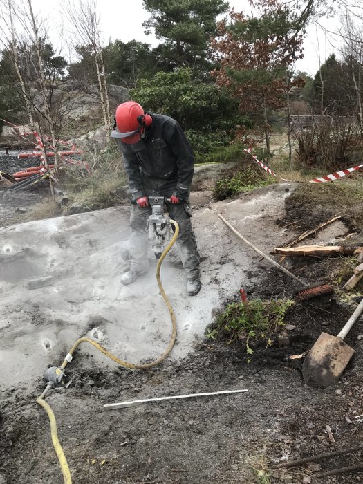 Person använder tryckluftsdriven bergborr för att borra hål i berg på en brant sluttning utomhus.