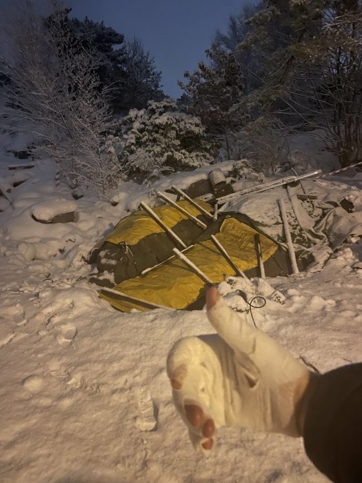 En snötäckt bergsknalle med borrade hål och dynamit i kvällsljus, med förgrunden visande en hand i trasig handske.