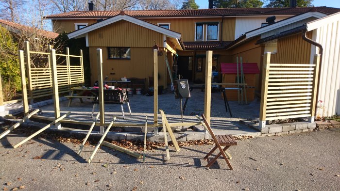 Pågående byggnation av trädgårdsstaket med tryckimpregnerat virke i olika stadier av färdigställande.