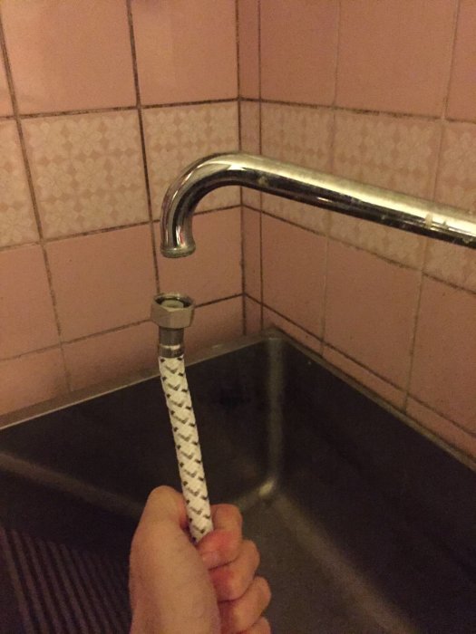 Hand som håller en duschslang intill en vattenkran där gängorna inte passar samman.