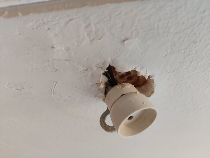 Takdosa med skadad kant, skarvade kablar fixerade med häftstift, och lock med krok.