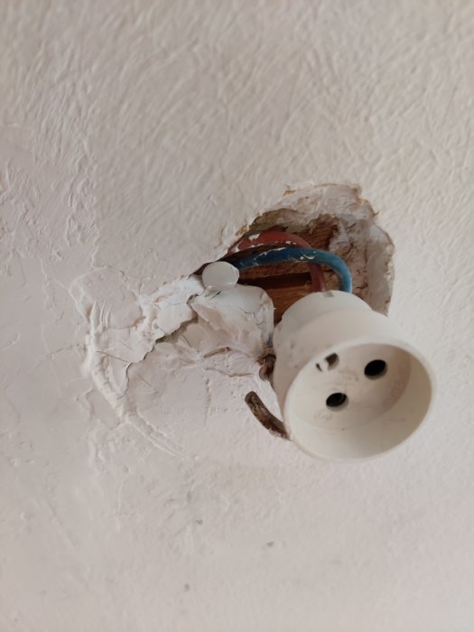 Takdosa med ojämnt spackel och en gammal kronkontakt, kablar skarvade med tejp och hålls på plats av ett häftstift.
