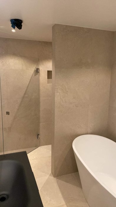 Modernt badrum under renovering med beige kakel, walk-in-dusch och frittstående badkar.