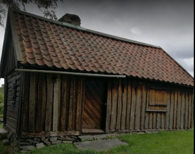 Ett gamla trähus från 1800-talet, med enkelt tak, och en stor öppen dörr, beläget i Partille.