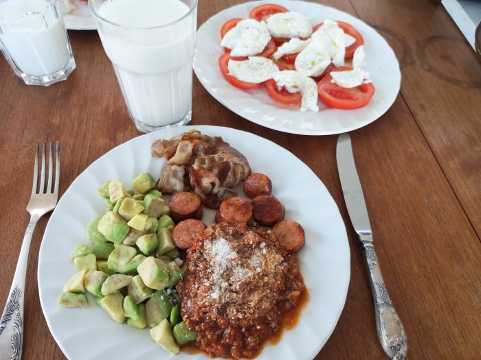 Måltid med köttbullar, hackad avokado, tomater och mozzarella, bacon och två glas mjölk.