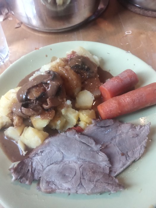 Tallrik med ugnstekt karré, kokt potatis, morötter och svampsås.