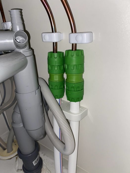 Rörinstallation under diskbänk med kopparledningar och gröna kopplingsdon.