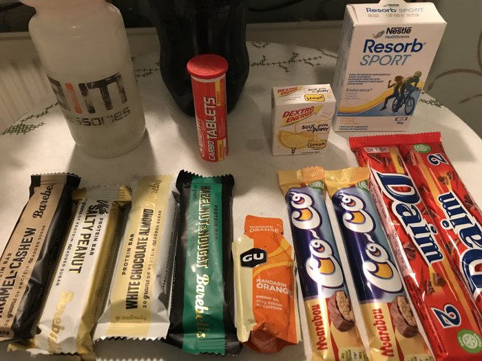 Olika energitillskott och snacks på ett bord, inklusive proteinbars, sportdryck och godis.