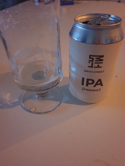 En tom ölglas bredvid en halvdrucken burk av Smith Street IPA på ett bord.