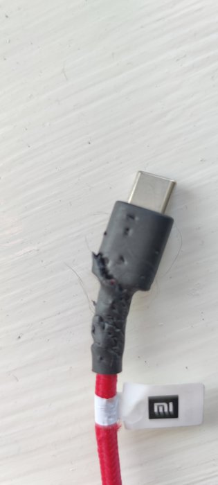 Skadad röd laddsladd med tydliga bett och trasig plast nära USB-kontakten.