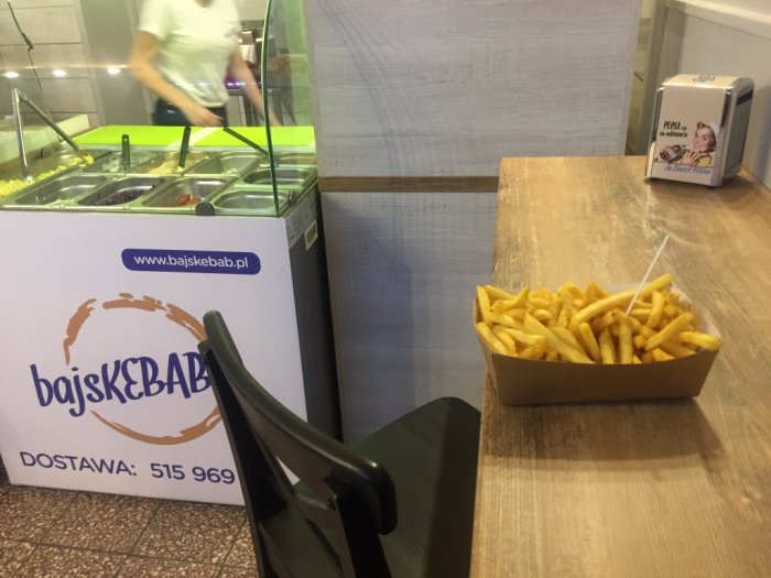 Pommes frites i en pappersförpackning på ett bord inne i en snabbmatsrestaurang.