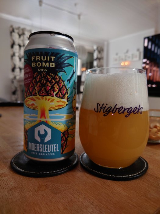 En burk Moersleutel Fruit Bomb DIPA bredvid ett fyllt ölglas märkt Stigbergets, på ett bord inomhus.