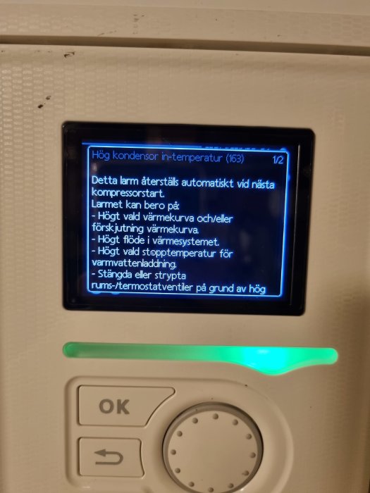 Display på värmesystem med felmeddelande om hög kondensortemperatur och knappsats nedanför.