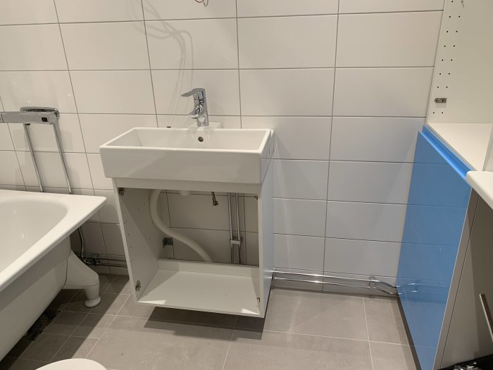 Ett nyrenoverat badrum med vit porslinsservant och synliga rör under som hindrar full öppning av högskåpets dörr.