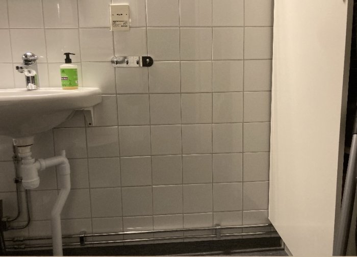 Badrum med rördragning som hindrar dörren från att öppnas helt, inklusive synligt dörrstopp.