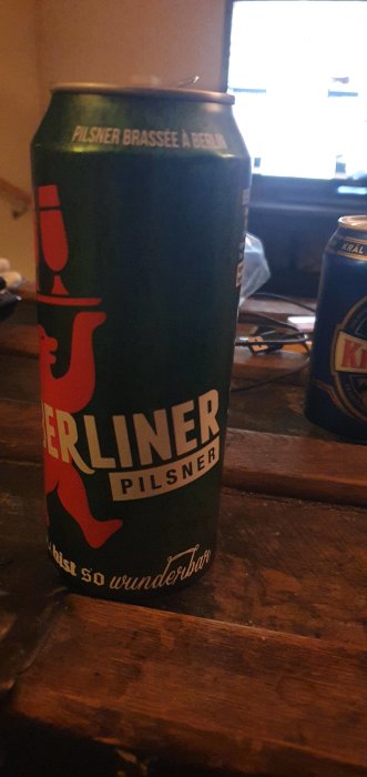 En Berliner Pilsner-öldosa på ett träbord med texten "Just so wunderbar!" samt en annan ölburk i bakgrunden.