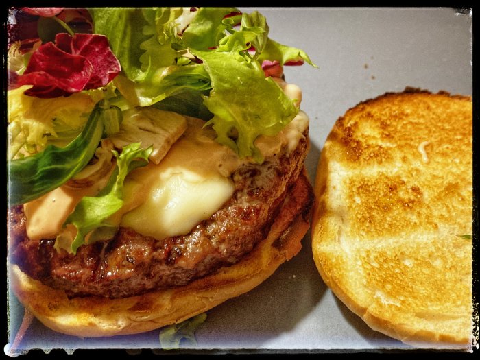 Grillad hamburgare med smält ost, sallad och bröd, lagom smält i grillat tillstånd.