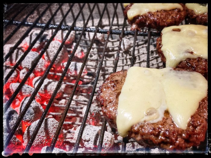 Hamburgare med smält ost som grillas över glödande kol på en grill.