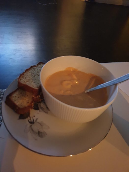 Skål med räksås som ser ut som soppa och en bit bröd på en tallrik.