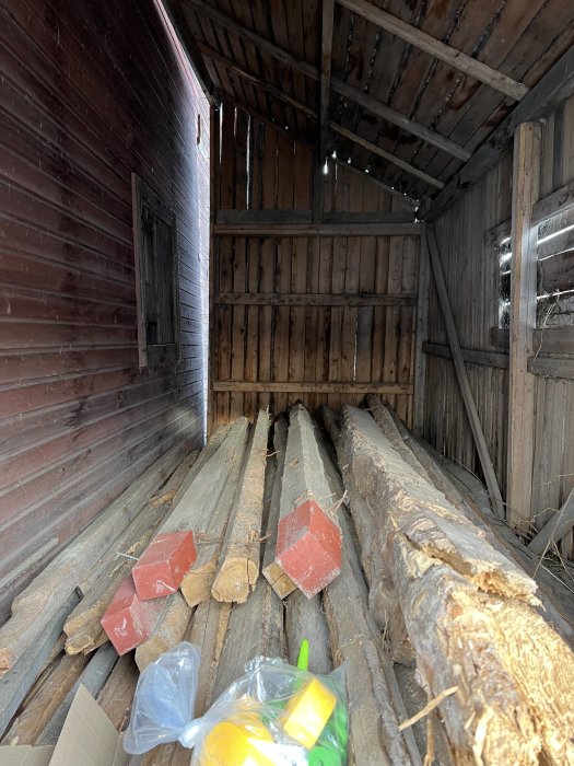 Inredning av äldre vedbod med träbjälkar och brädor, potentiellt för omvandling till växthus.