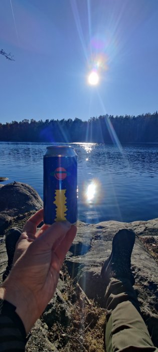 Person som håller en dryckesburk medan de sitter på en klippa vid vattnet en solig dag i skärgården.