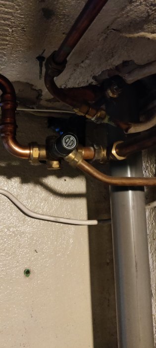 VVS-installation med kopparledningar och en manometer under en betongtak.