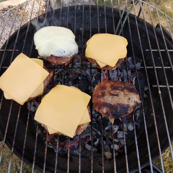 Hamburgare med smält ost grillas över kol på en grill.