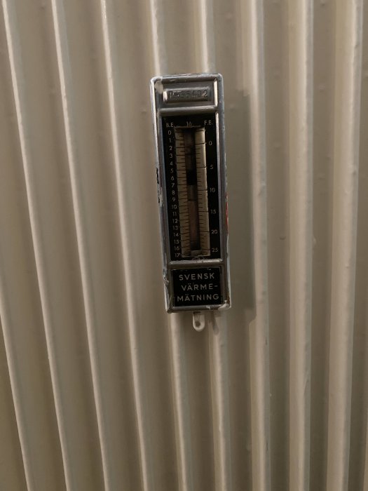 Närbild av en termometer med texten "SVENSK VÄRME MÄTNING" på ett radiatorselement.