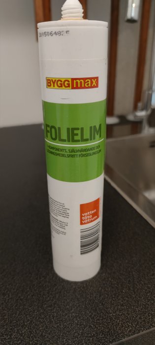 Tub med folielim från Byggmax för lagning, självhärdande och vattentätt, står på mörk bakgrund.