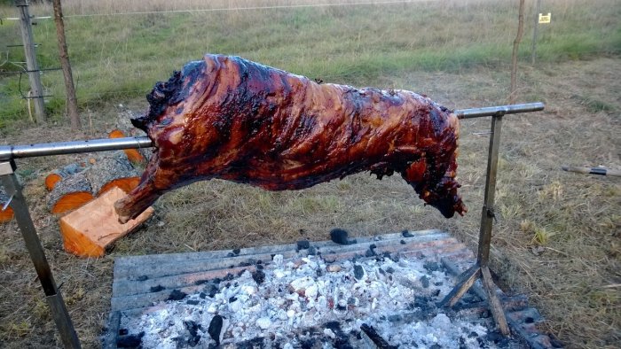 Ett grillat vildsvin roterar på en spett över glödande kol utomhus.