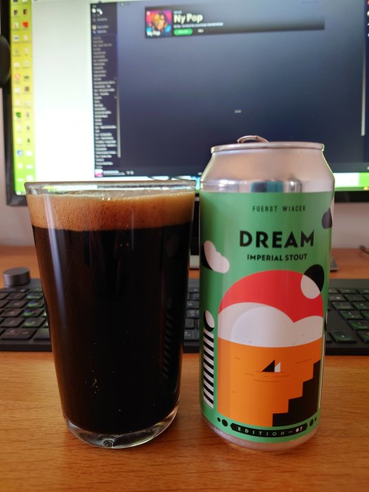 Ett glas mörk öl bredvid en burk Fuerst Wiacek Dream Imperial Stout på ett skrivbord.