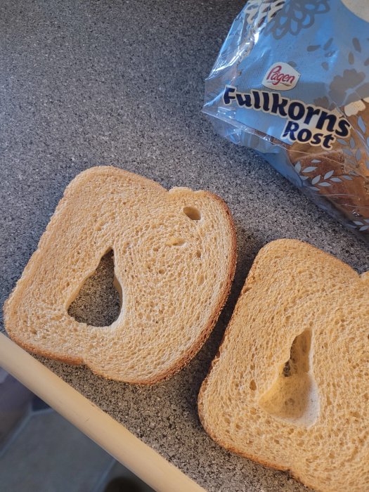 Två skivor fullkornsbröd på en köksbänk bredvid en brödpåse med texten "Fullkorns Rost".