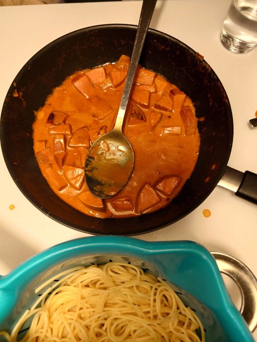 Stekpanna med kryddstark stroganoff och bitar av falukorv serverad med spagetti i en blå skål.