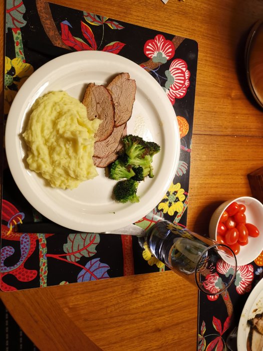 Grillad fläskytterfilé med potatismos och broccoli på en tallrik, serverad på ett blommigt bord.