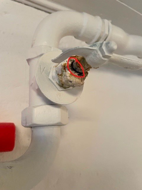 Läckage vid skruven på en gammal vitmålad radiatorventil markerat med en röd cirkel.