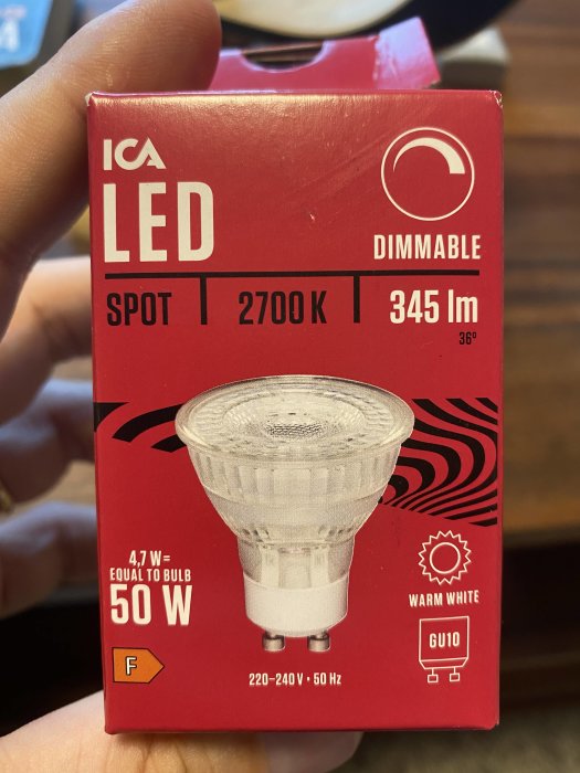 Hand håller en förpackning för ICA dimbar LED-spotlampa, 2700 K, 345 lm, 4,7 W motsvarande 50 W.