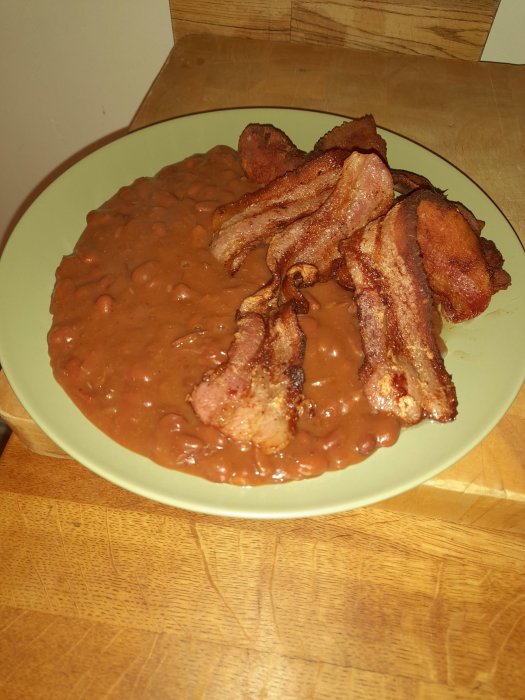 En tallrik med bönor och stekt bacon på en träyta.