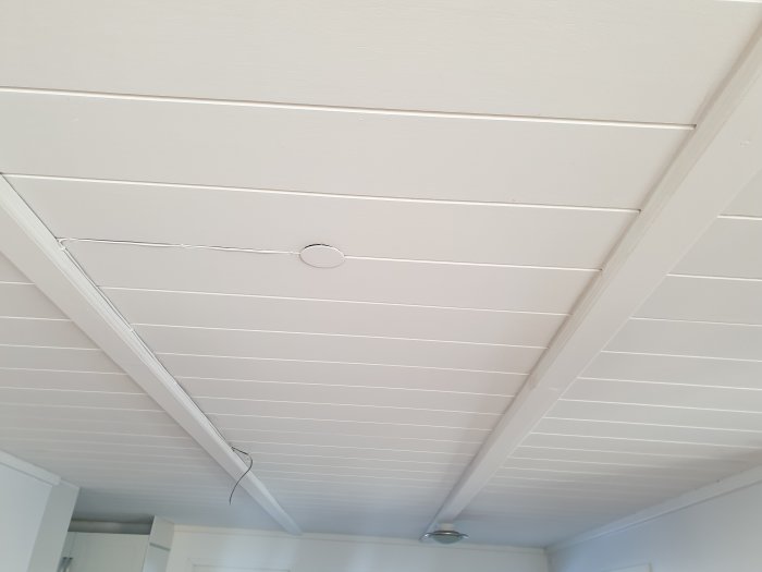 Vitmålat träpaneltak med en synlig elektrisk kabel och installationsring.
