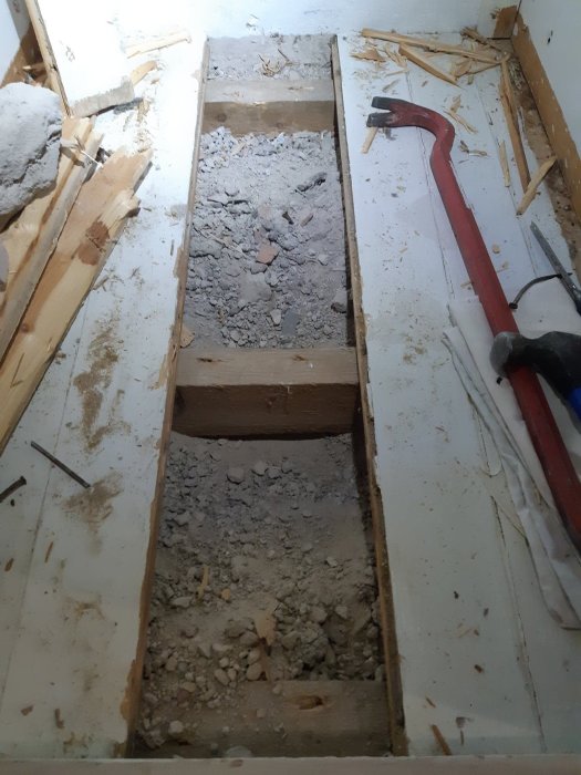 Öppet golv med synliga träreglar och murbruk, samt verktyg för renovering, i en bostad under ombyggnation.